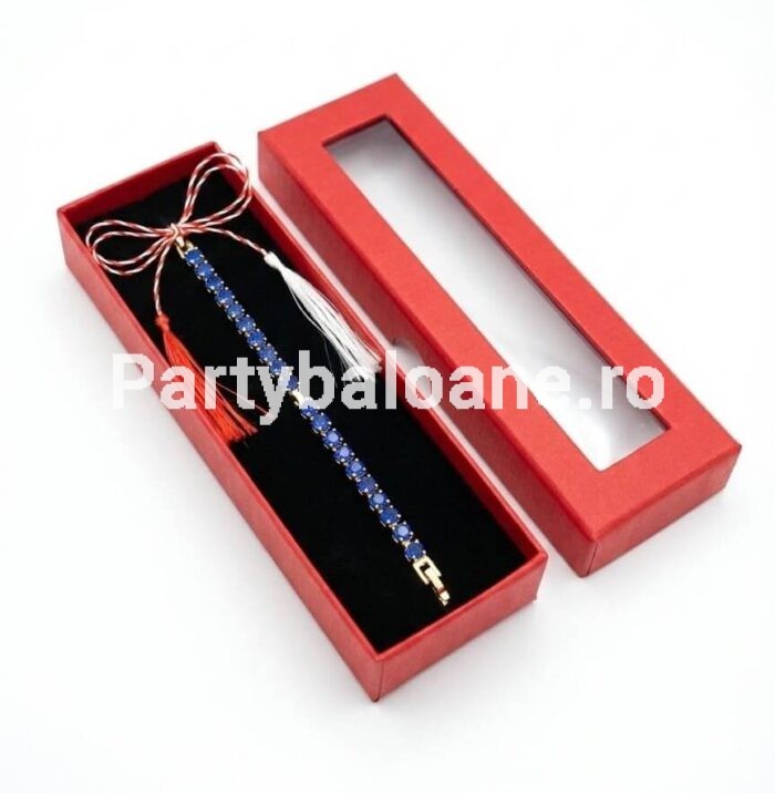 Mărțișor Premium Brățară Strasuri Albastre – Cadou Elegant (Cutie Inclusă) Mărțișor premium brățară elastică aurie cu strasuri albastre așezată în cutie lungă roșie de cadou cu fereastră și șnur alb-roșu de 1 Martie.