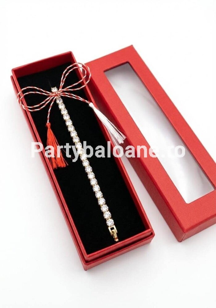 Mărțișor Premium Brățară Strasuri – Cadou Elegant 1 Martie (Cutie Inclusă) Mărțișor premium brățară elastică aurie cu strasuri clare strălucitoare așezată în cutie lungă roșie de cadou cu fereastră și șnur alb-roșu de 1 Martie.